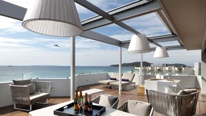 A spacious outdoor deck with modern furniture, a tray with bottles, and a view of the sea. - Hotel Garbi Ibiza & Spa (Sant Josep de sa Talaia)