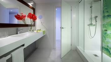 A modern bathroom with a large mirror, a sink with two clear glasses, a vase with red flowers, and a shower area with a glass door.