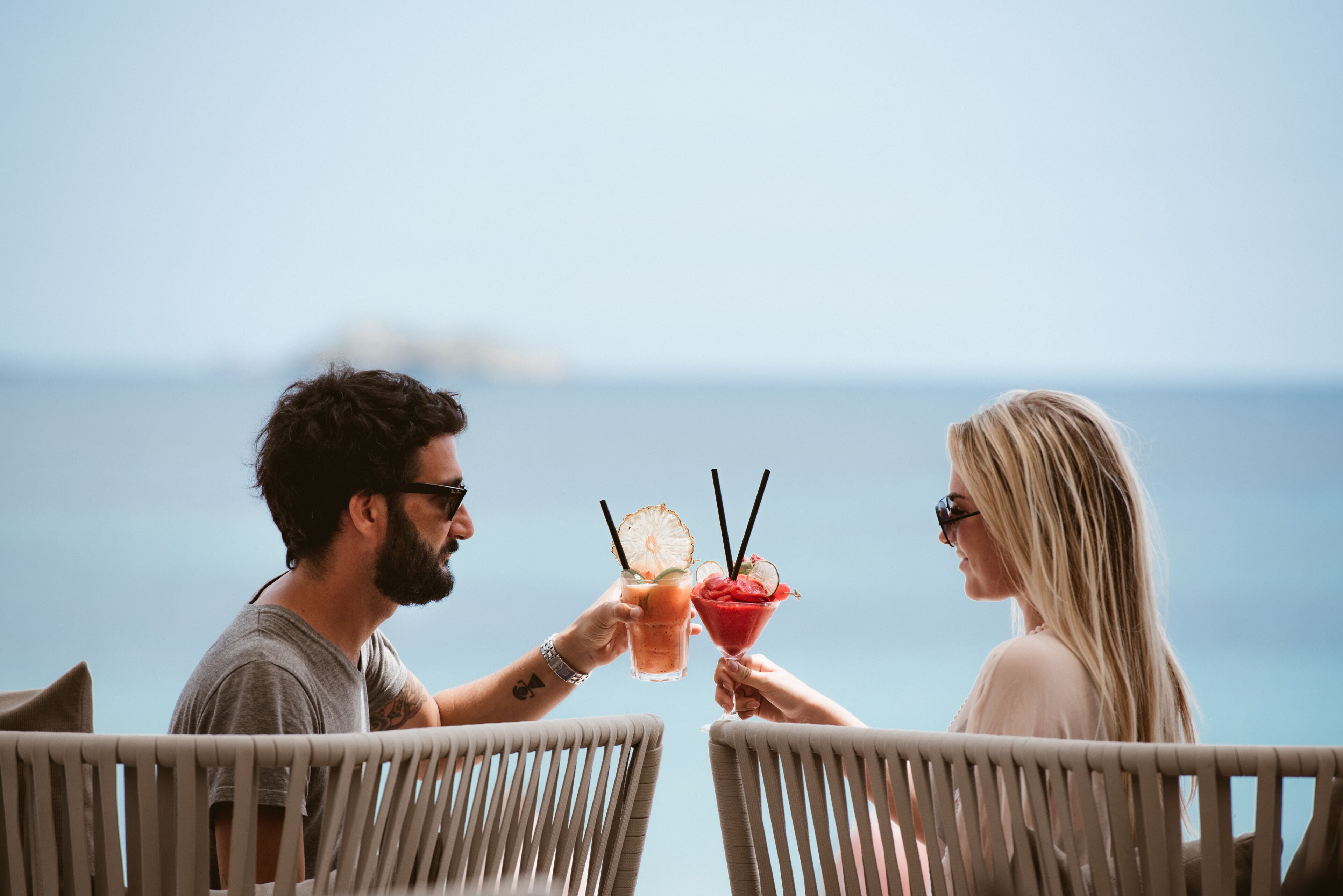 Two people toasting with drinks in a seaside setting, overlooking the ocean.