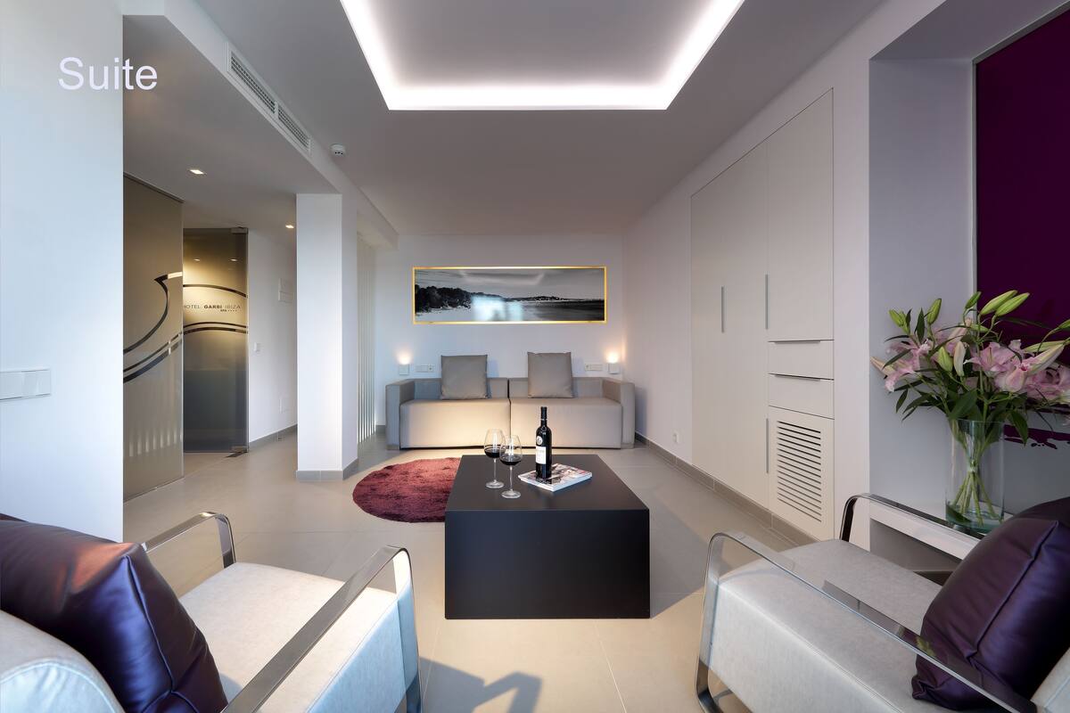 A modern suite with a black coffee table, two wine glasses, a bottle, a sofa, and a large window with a cityscape view.