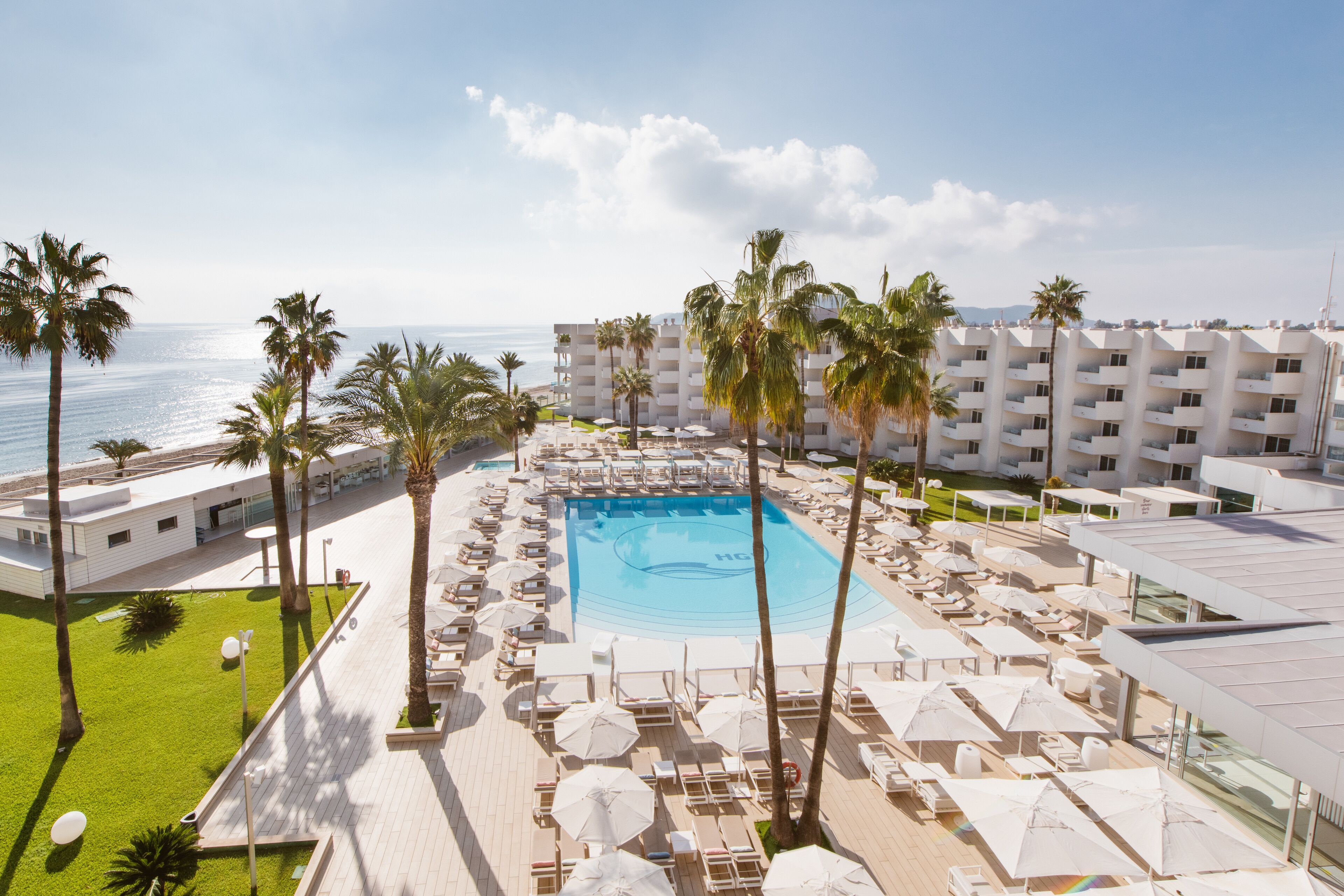 A resort pool area with sun loungers, umbrellas, and palm trees.