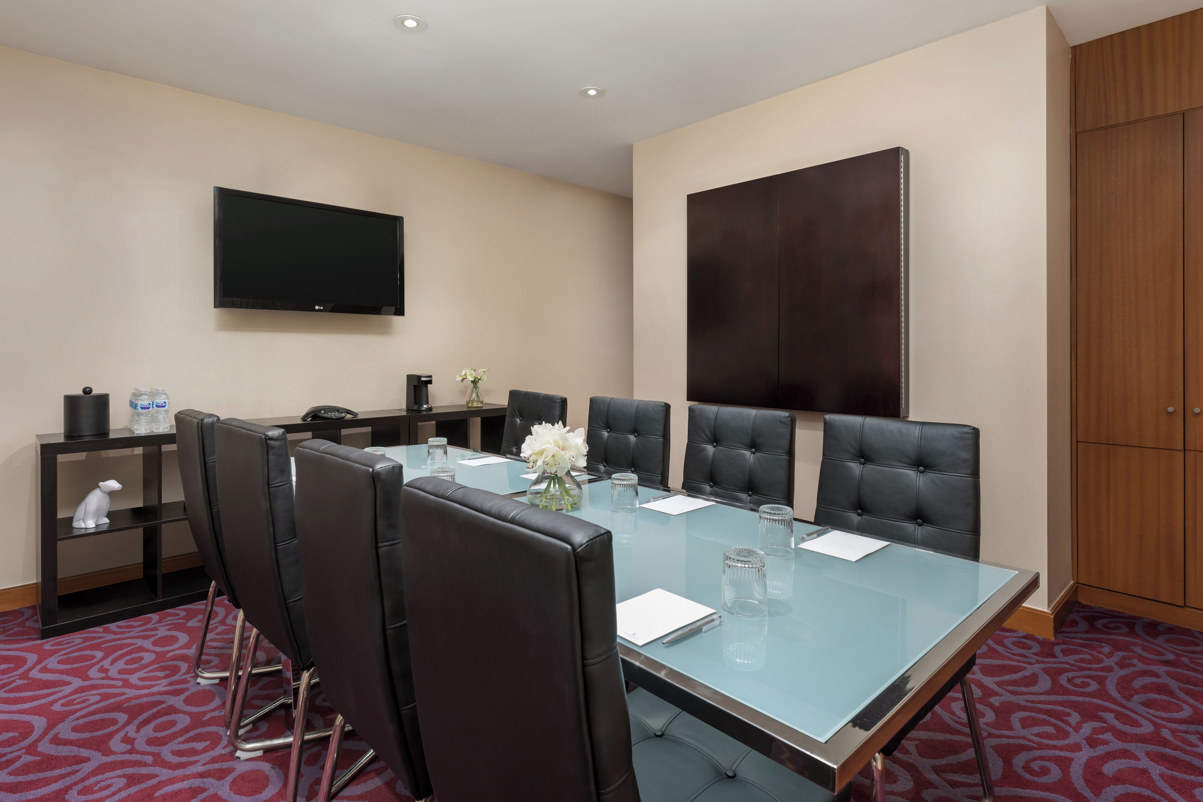 Une salle de conférence dotée d’une table en verre, de fauteuils en cuir noir, d’un téléviseur à écran plat et d’une grande œuvre d’art aux couleurs sombres accrochée au mur.
