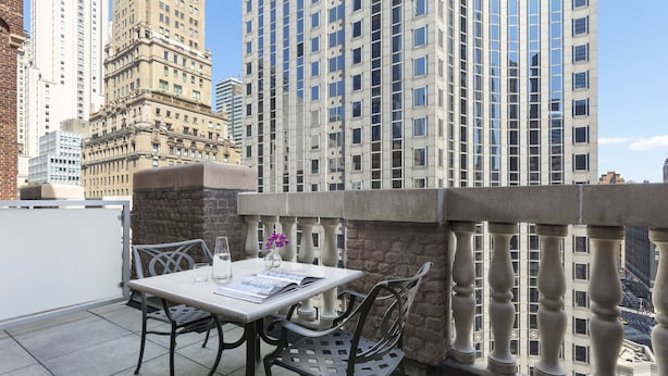 An outdoor balcony with a table and chairs, a stone pillar, and a view of tall buildings. - Hotel 57 (New York)