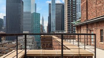 Une vue urbaine avec des gratte-ciel modernes et un bâtiment en briques doté d’une rambarde métallique au premier plan.