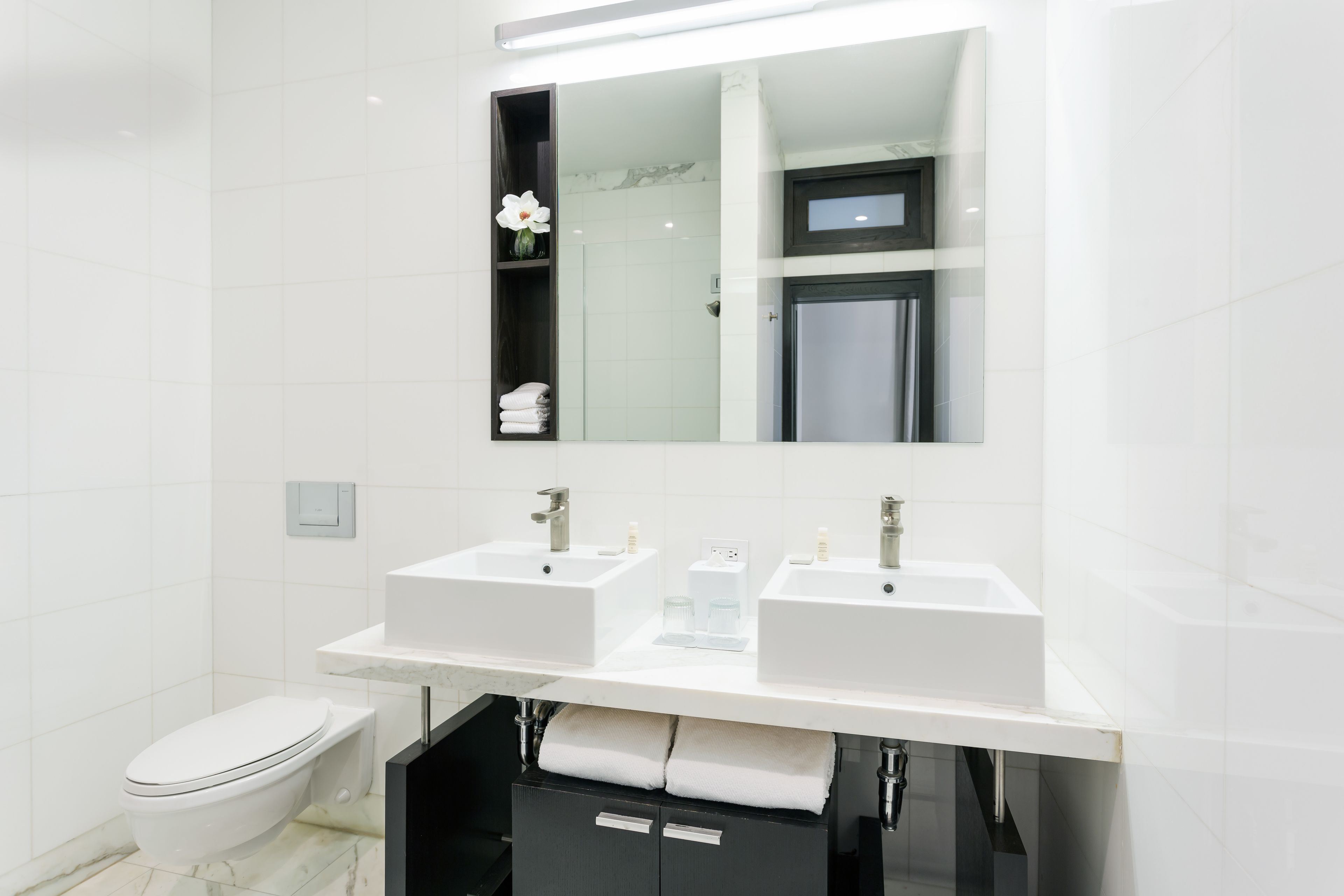 A modern bathroom with two sinks, a toilet, and a mirror above the sink.