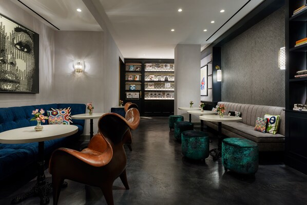 A modern interior with a blue sofa, leather chairs, teal ottomans, and a wall with framed pictures. - Hotel 57 (New York)