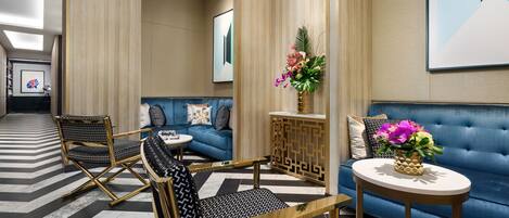 A modern lobby with a blue sofa, black and gold chairs, a small round table, and a decorative plant.