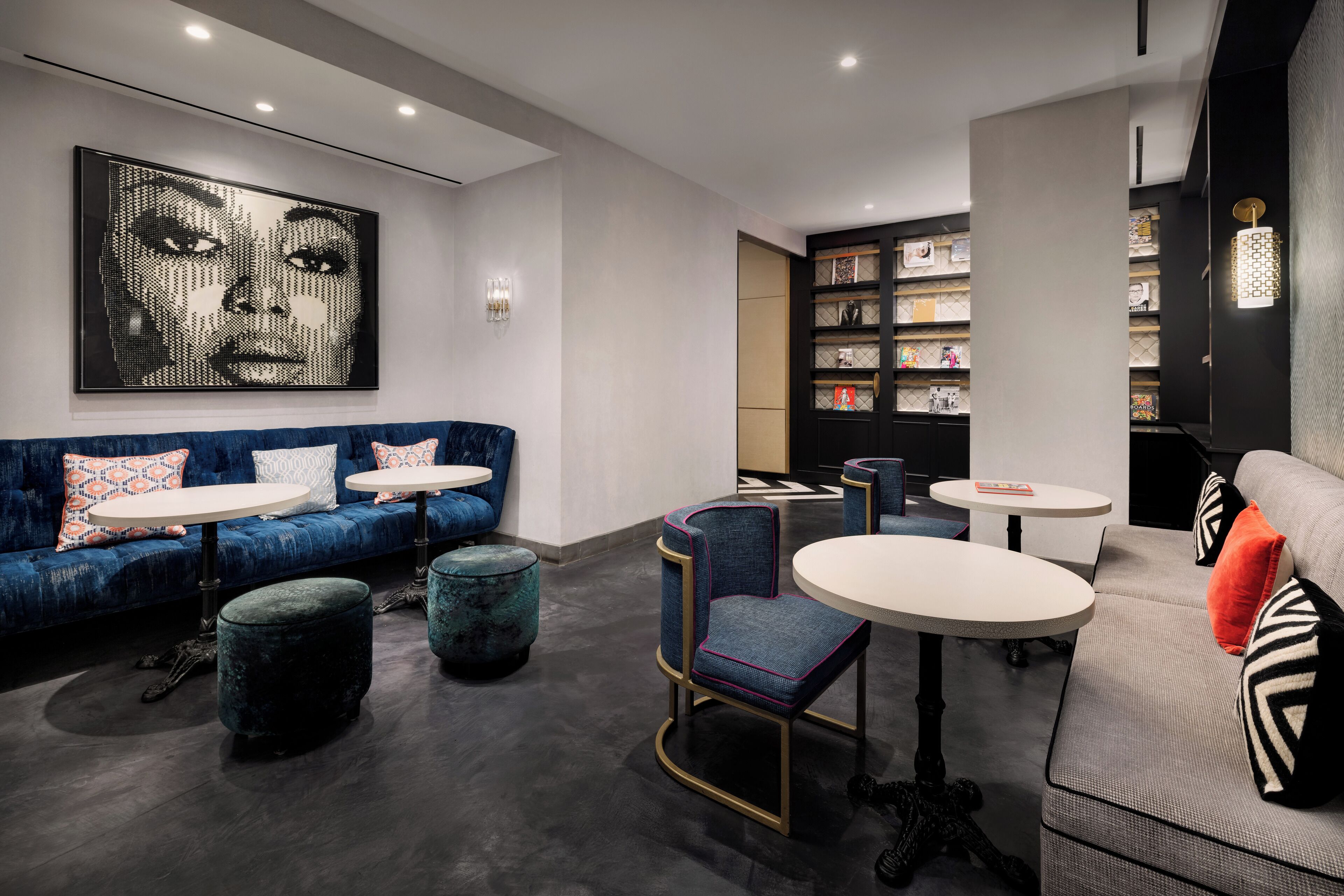 A modern lounge area with a blue sofa, round tables, and a bookshelf.