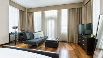 A modern hotel room with a large bed, a sofa, a desk with a computer, a TV, and a large window with curtains.