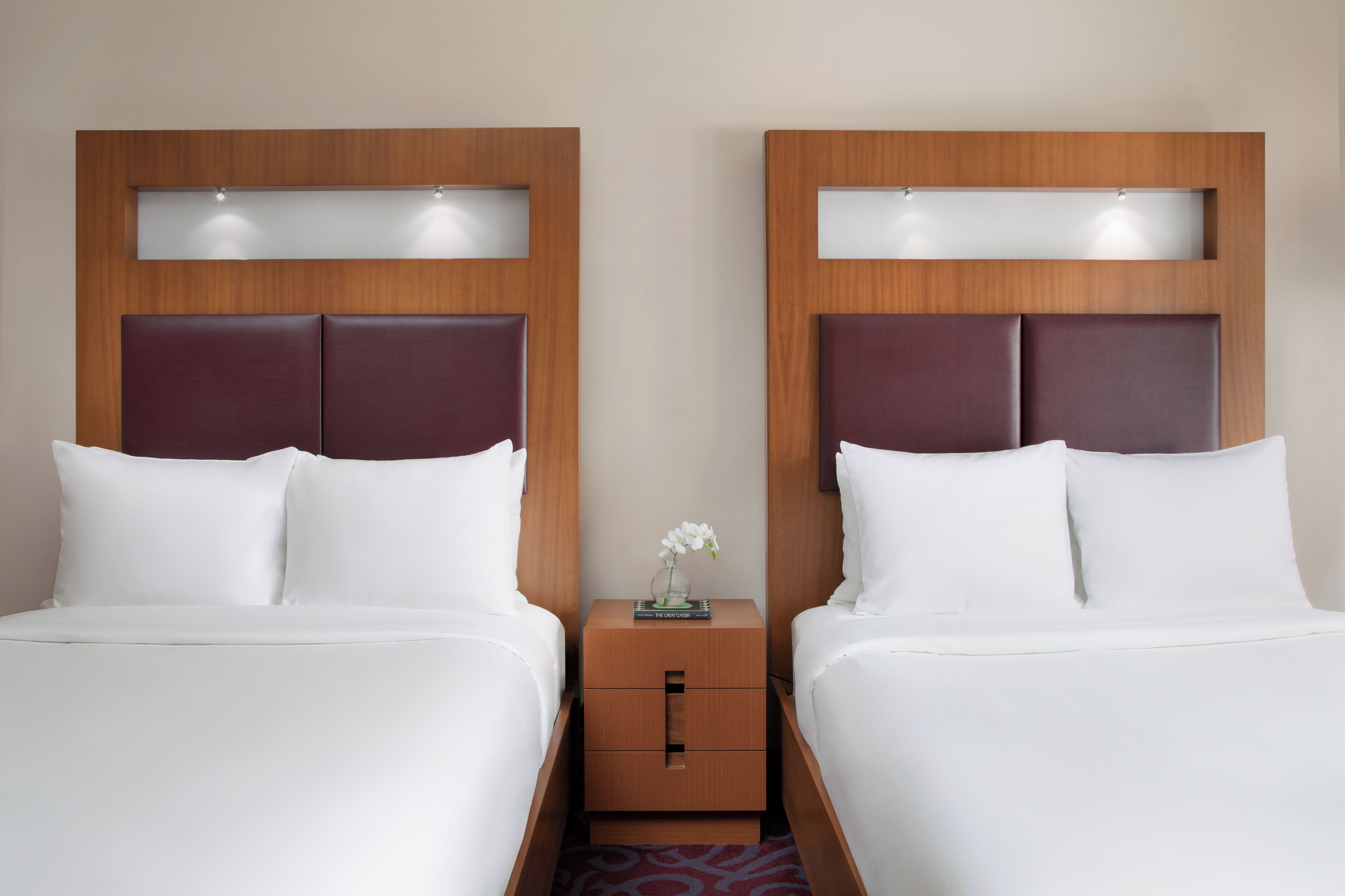 A hotel room with two beds, each with a wooden headboard and a small nightstand between them.