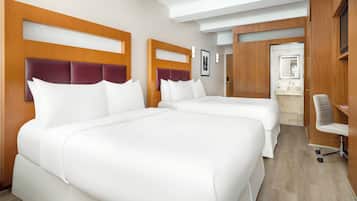 A hotel room with two large beds, a wooden headboard, a desk, and a bathroom with a sink and mirror.