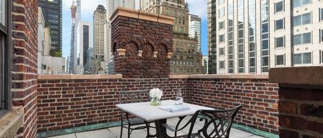 Una terraza en la azotea con un muro de ladrillo, una mesa, dos sillas y una planta en maceta.