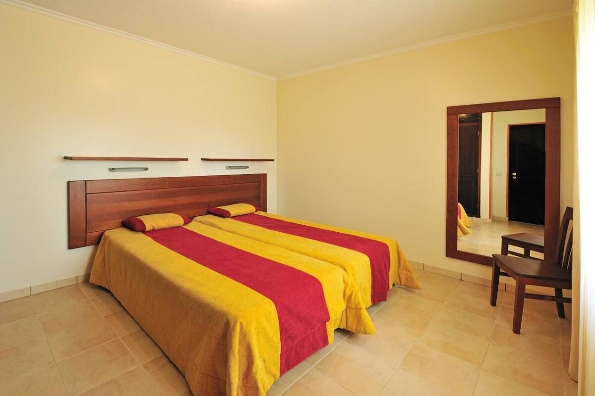 Une chambre avec deux lits, une tête de lit en bois, un miroir et une chaise.