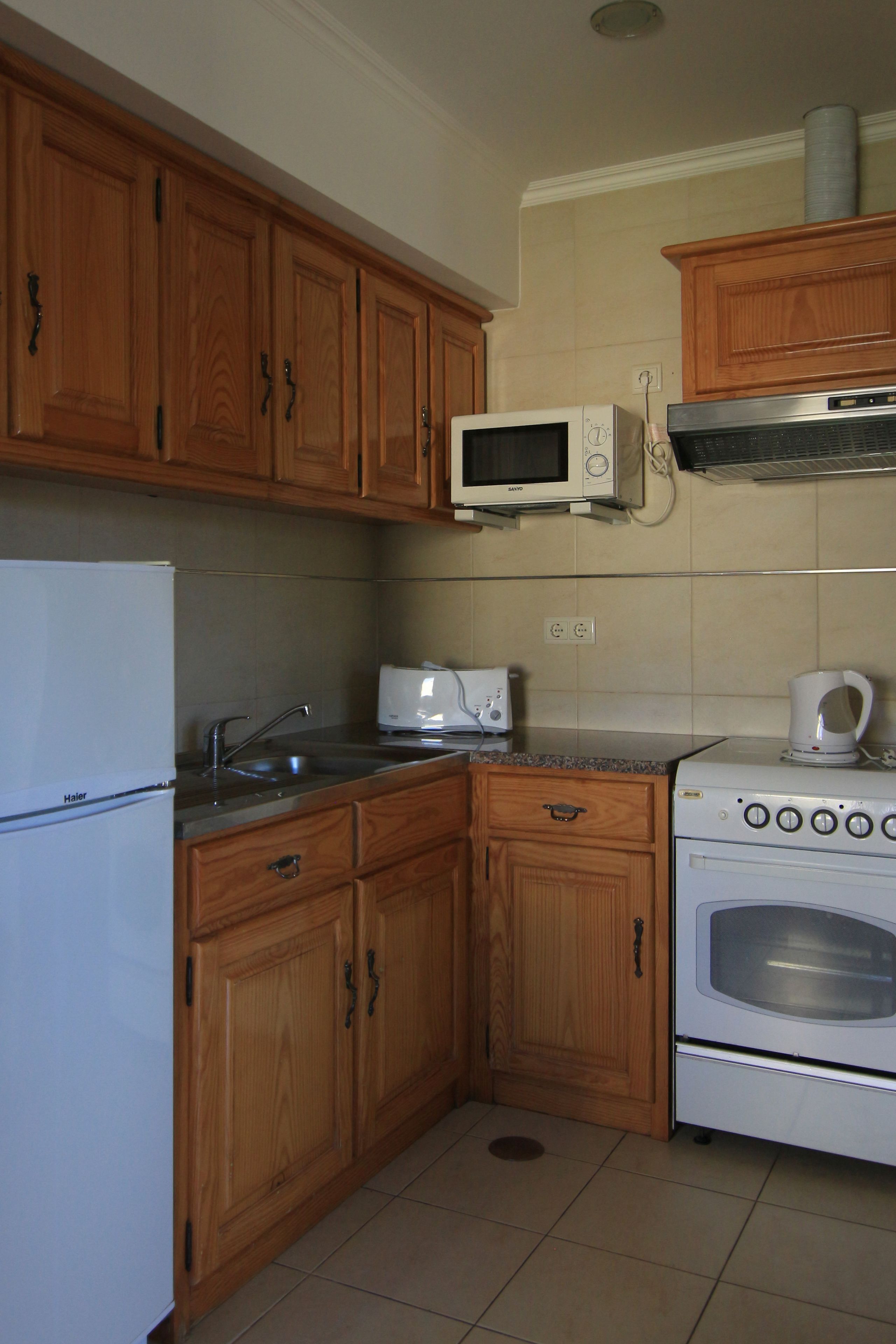 Una cocina con armarios de madera, un refrigerador blanco, un microondas, un tostador y un horno.