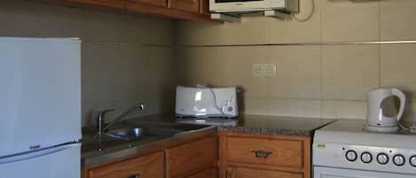 Una cocina con armarios de madera, un refrigerador blanco, un microondas, un tostador y un horno.