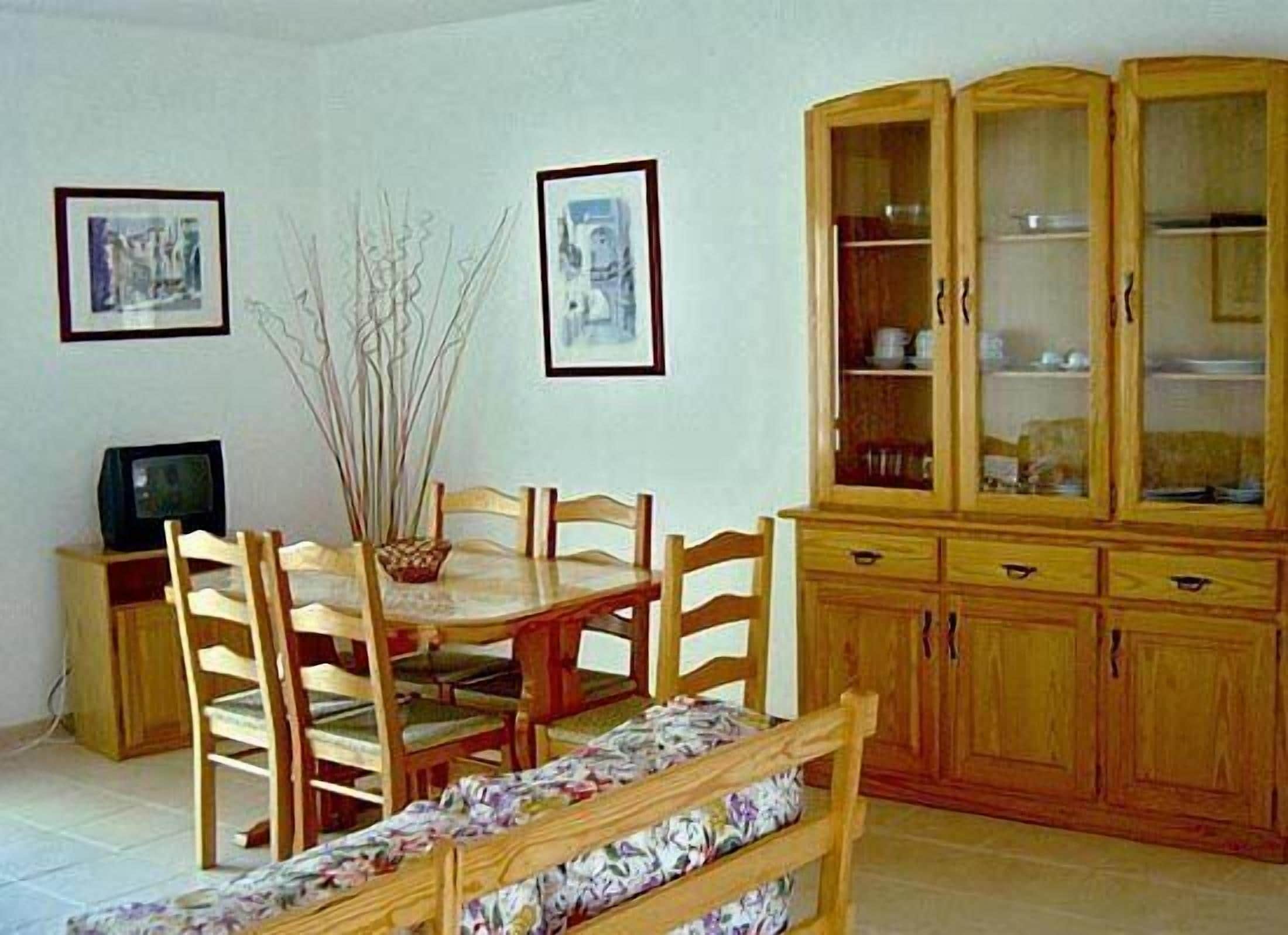 Ein Essbereich mit Holztisch, Stühlen, einer Bank, einem Schrank mit Glastüren und zwei gerahmten Bildern an der Wand.