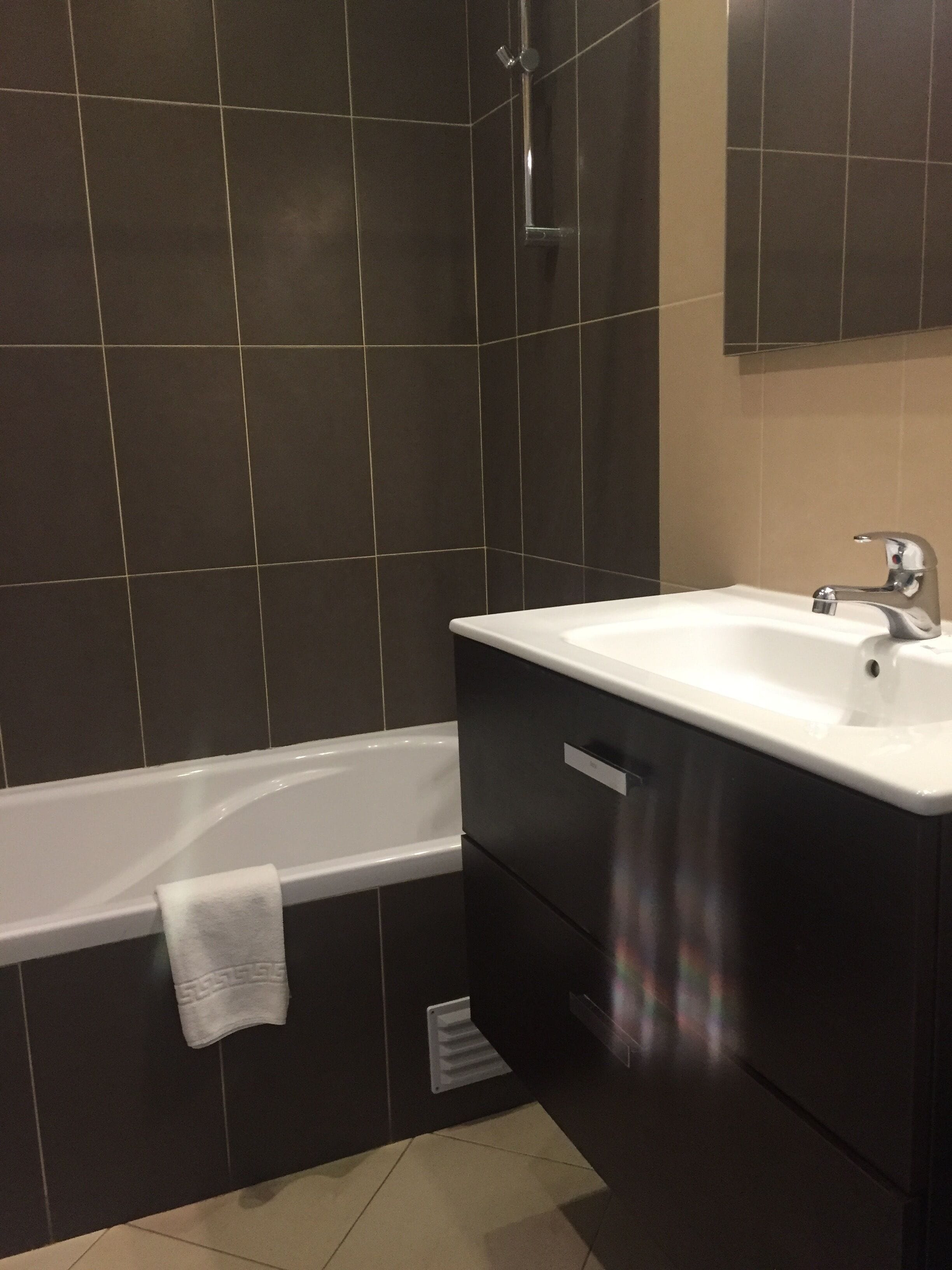 A modern bathroom with a bathtub, a white sink, dark cabinetry, and a mirror above the sink.