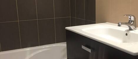 A modern bathroom with a bathtub, a white sink, dark cabinetry, and a mirror above the sink.