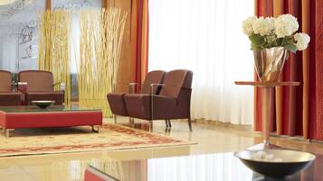 A modern lobby with a red sofa, a glass coffee table, and a vase of white flowers on a stand.