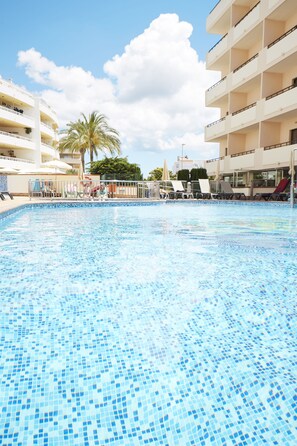 A swimming pool with lounge chairs and umbrellas, surrounded by multi-story buildings with balconies.