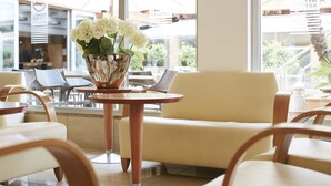 A modern indoor seating area with a table and chairs, a vase with white flowers, and large windows offering a view of the outside. - Invisa Hotel La Cala (Santa Eulalia del Rio)