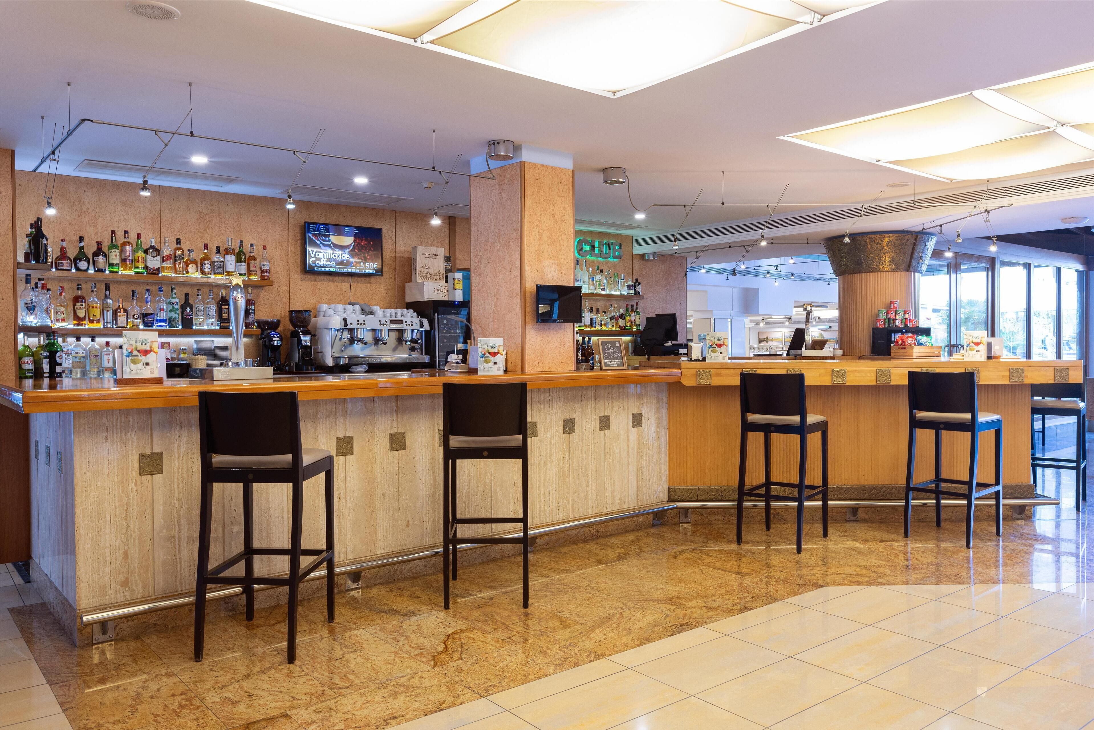 A bar area with a counter, bar stools, and shelves of beverages.