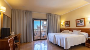 A hotel room with a bed, a desk with a chair, a television, and a balcony with curtains. - Invisa Hotel La Cala (Santa Eulalia del Rio)
