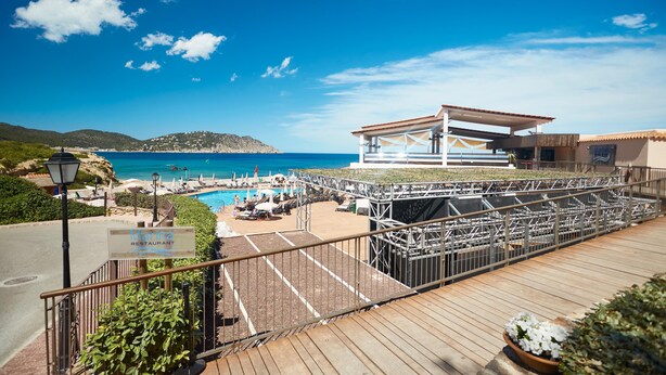 Zona d'una piscina al terrat amb vista al mar, un rètol de restaurant i una zona d'estar coberta.