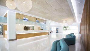 Una zona d'entrada moderna amb un taulell de recepció de fusta, una sala d'espera amb sofàs color cel i un gran finestral que aporta llum natural.