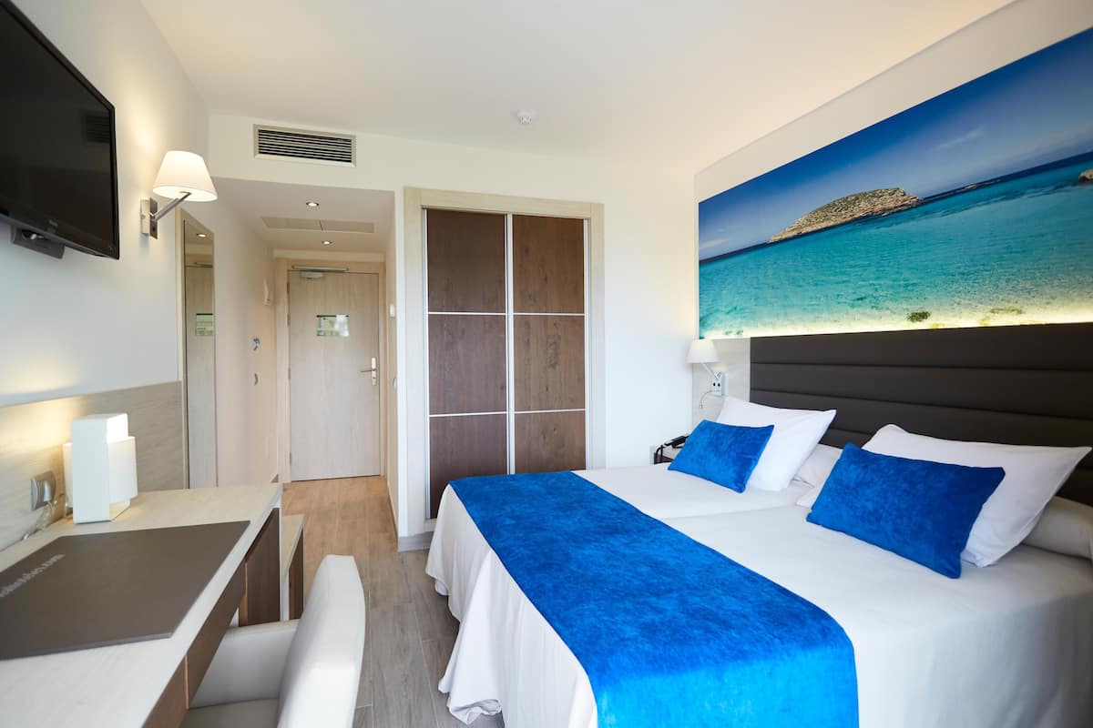 Une chambre d’hôtel avec un lit, un bureau, une télévision et un tableau représentant une plage.