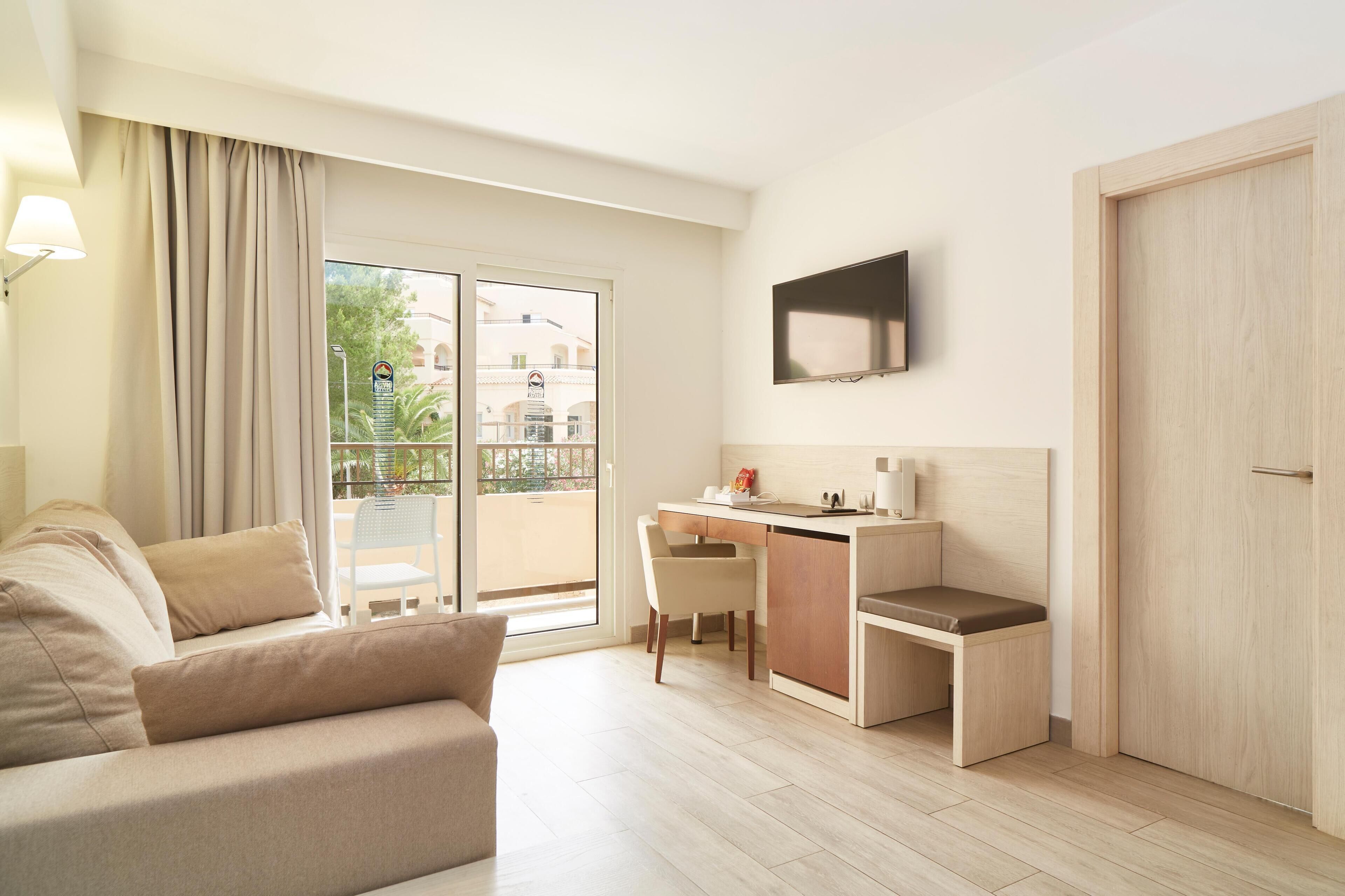 Une chambre d’hôtel moderne équipée d’un canapé, d’un bureau, d’une chaise, d’une télévision et d’une porte-fenêtre coulissante donnant sur le balcon.