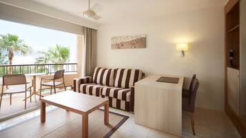 Una sala moderna con sofá, una mesa de comedor y sillas. Hay un balcón con vistas a palmeras y al mar.