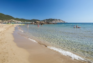 Enjoy the serene beach setting with clear, shallow waters and a picturesque rocky outcrop.
