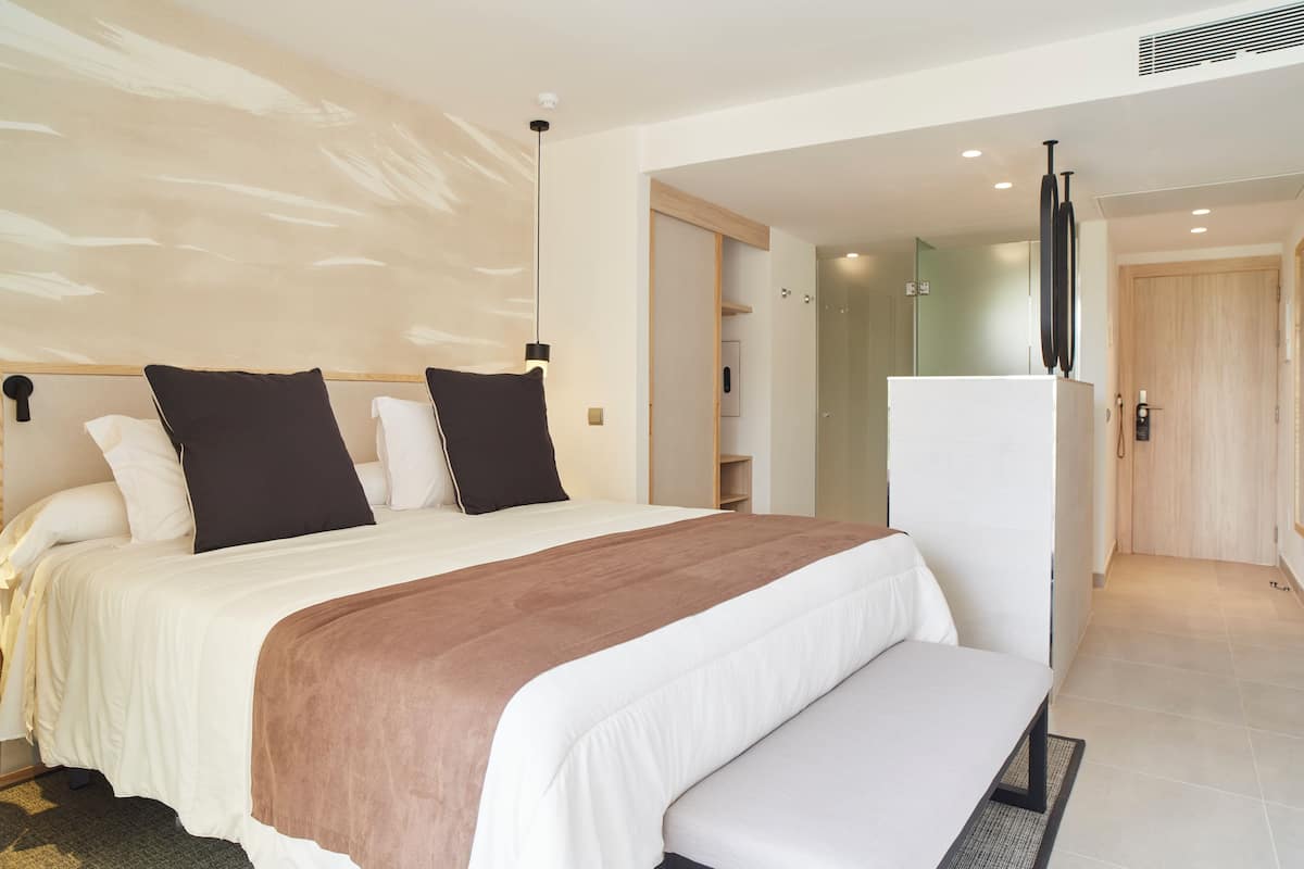 Une chambre d’hôtel moderne avec un grand lit, un banc, une armoire et un miroir.