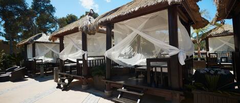 A series of thatched-roof outdoor seating areas with white canopies, wooden benches, and a paved walkway.