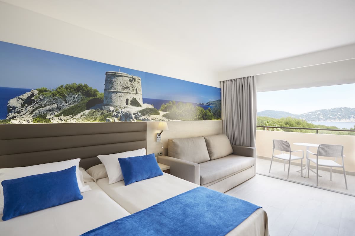 Une chambre d’hôtel avec un grand lit, un canapé et un balcon offrant une vue sur la mer et un château.