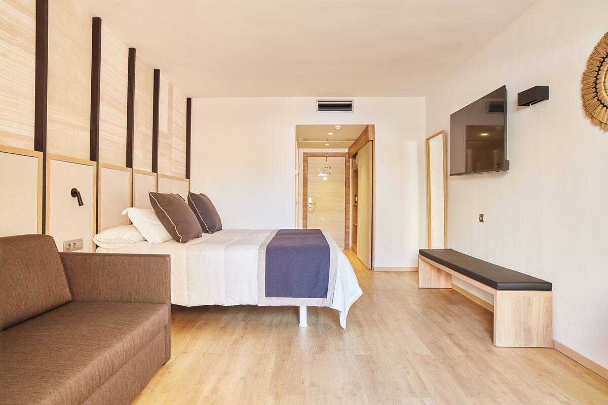 Une chambre d’hôtel moderne équipée d’un lit, d’un banc, d’une télévision et d’un plancher en bois.