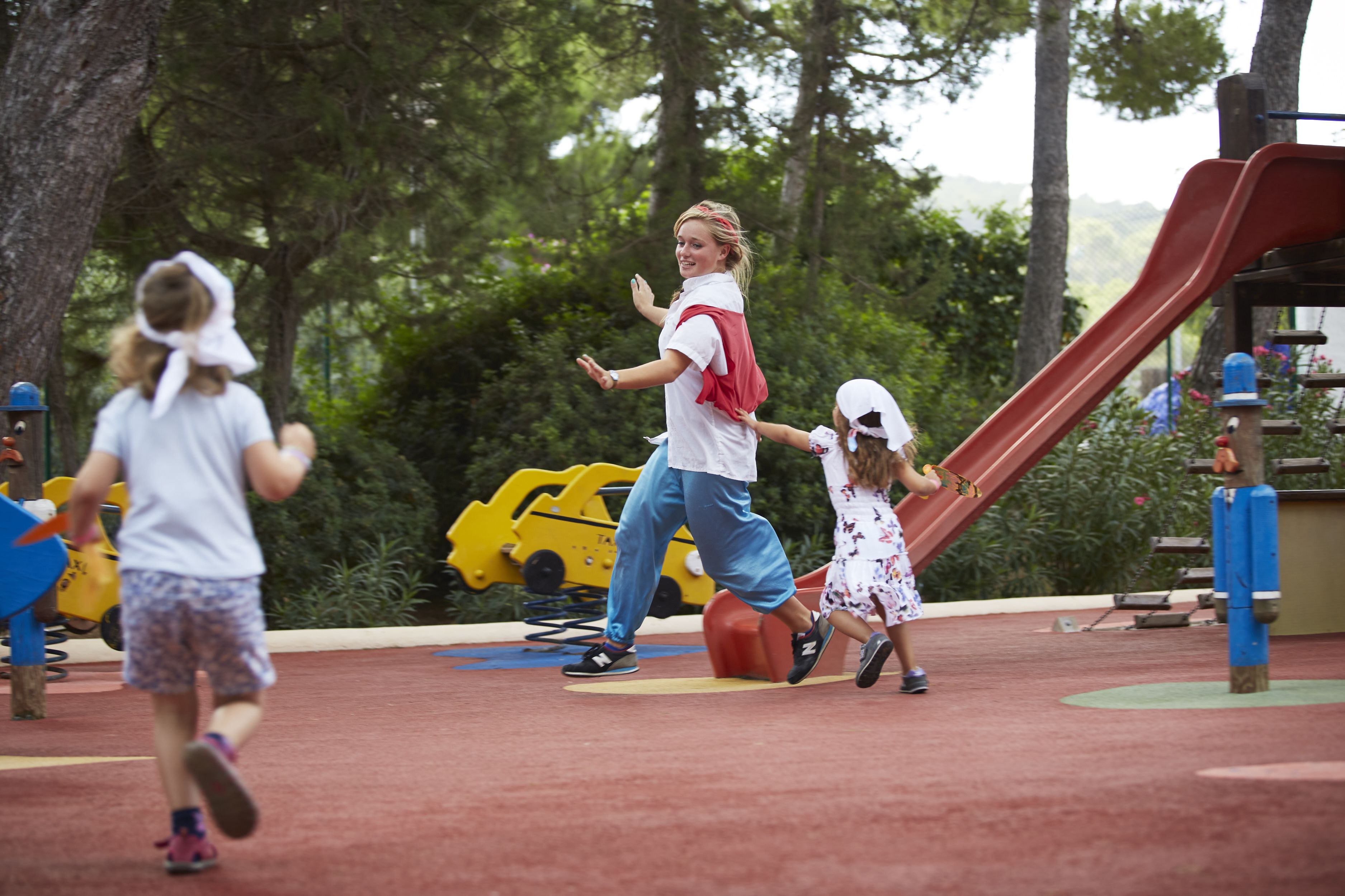 A playground with a slide, yellow toy cars, and trees in the background.