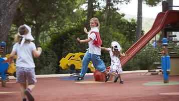 A playground with a slide, yellow toy cars, and trees in the background.