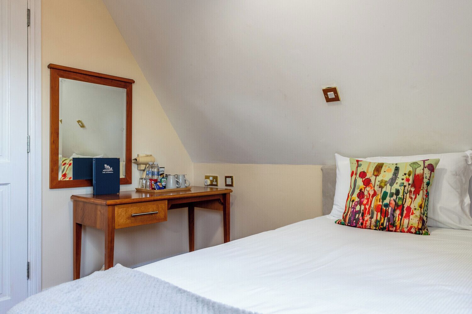 Un dormitorio con una cama, un escritorio de madera, un espejo y una mesita de noche con artículos de aseo.