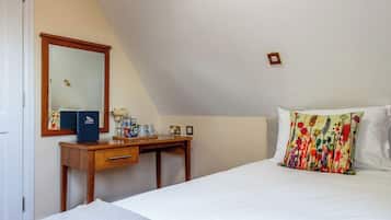 Un dormitorio con una cama, un escritorio de madera, un espejo y una mesita de noche con artículos de aseo.