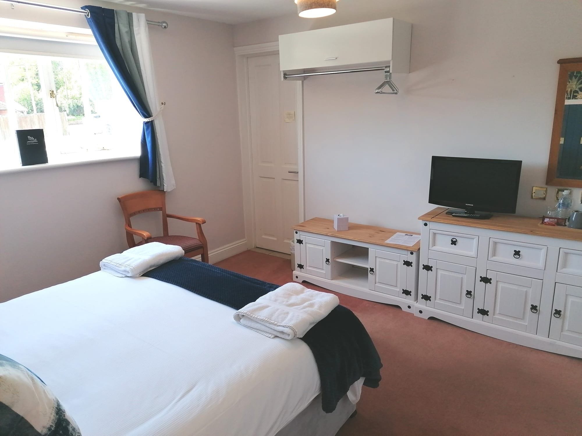 A hotel room with a bed, a chair, a TV, and a wardrobe.