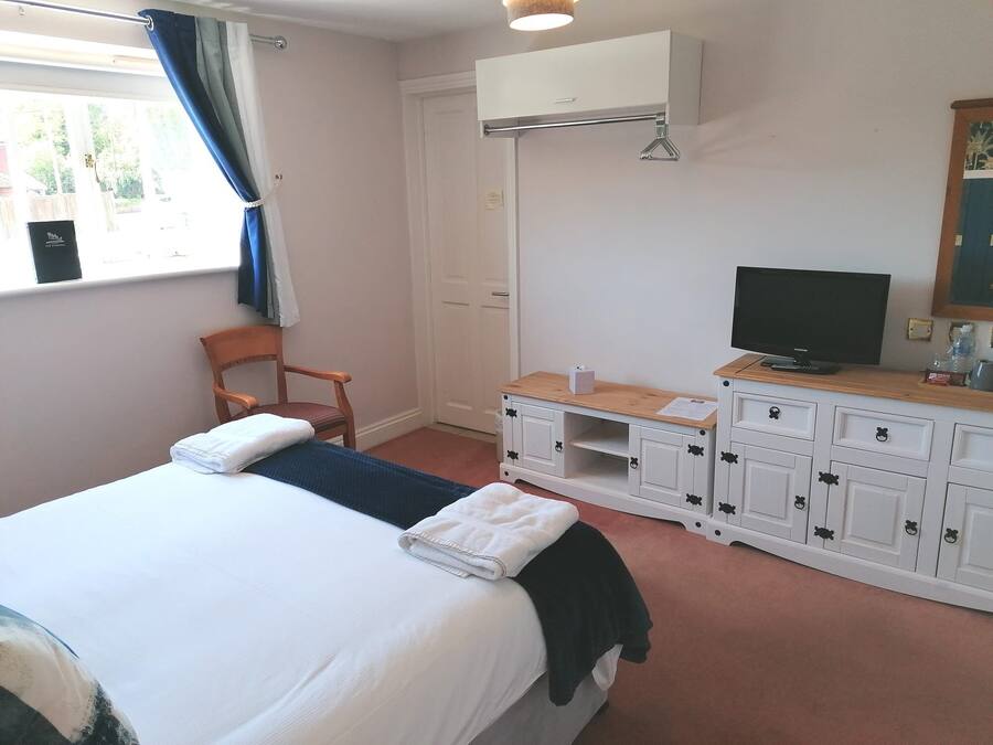 A hotel room with a bed, a chair, a TV, and a wardrobe.