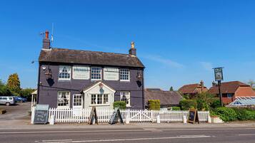 A two-story pub with a white picket fence in front, a signboard advertising Sunday dinner, and a clear blue sky.