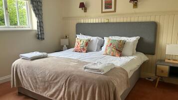 A neatly made bed with a grey headboard, white linens, and colorful pillows. There are two bedside lamps, a framed picture on the wall, and a window with curtains.