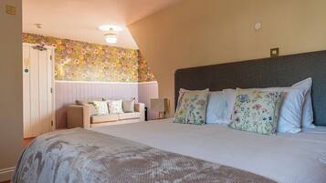 A bedroom with a large bed, a sofa, a nightstand, and a floral-patterned wall.