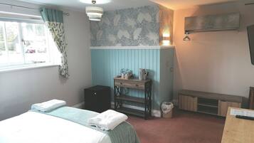 A bedroom with a bed, a desk, a chair, a radiator, and a window.