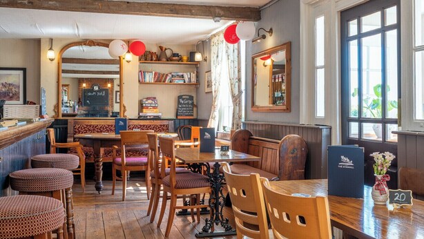 A cozy restaurant with wooden furniture, a bar area, and a bookshelf with books and decorative items. - The Evenhill (Canterbury)