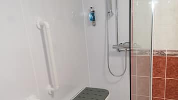 A shower area with a glass door, a white towel rack, a small step stool, and a handheld showerhead.