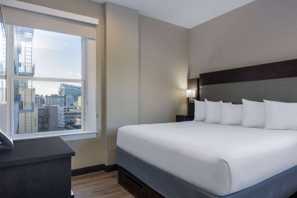 A hotel room with a large bed, a desk, and a window offering a city view.
